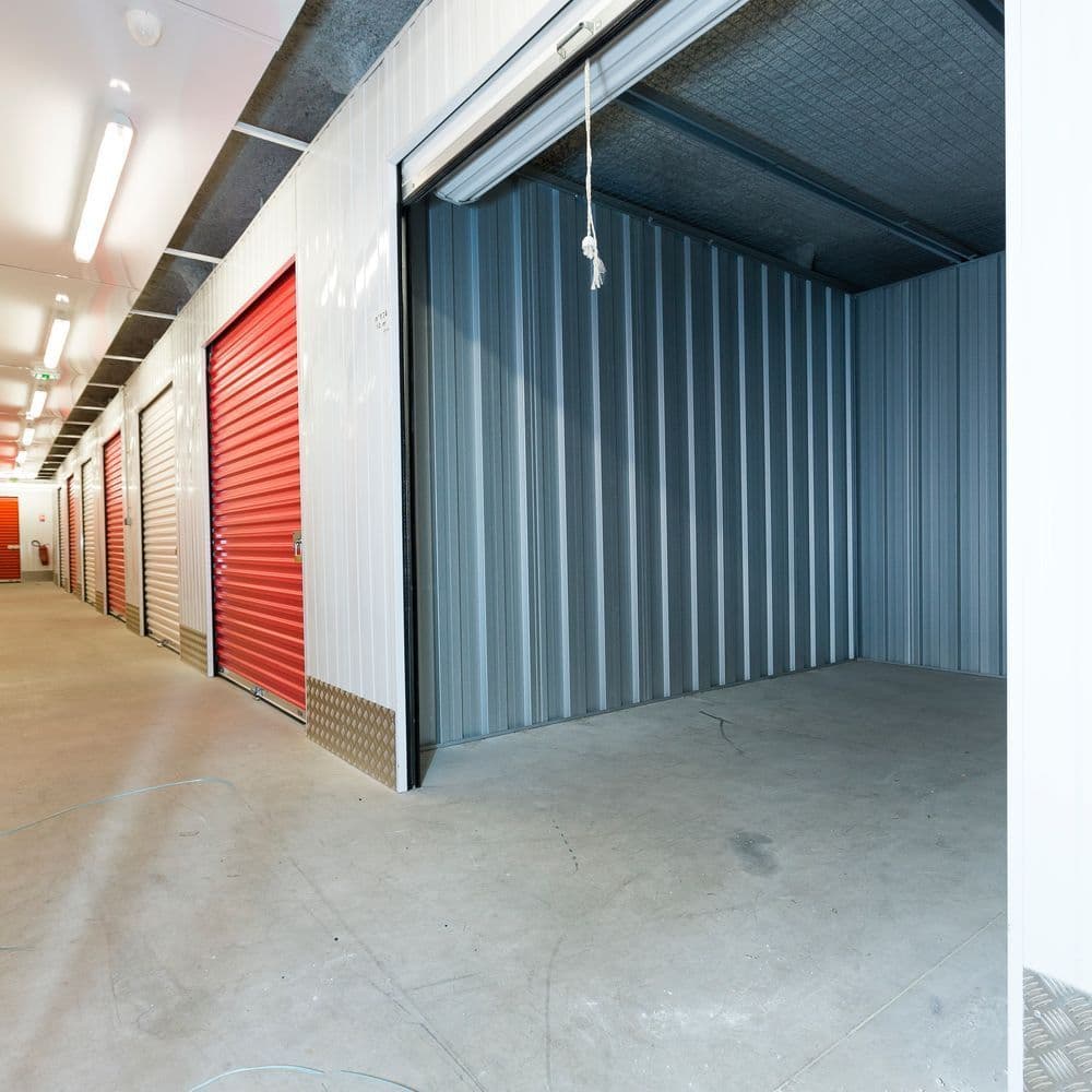 Interior corridor with red roller doors and an open empty self-storage unit