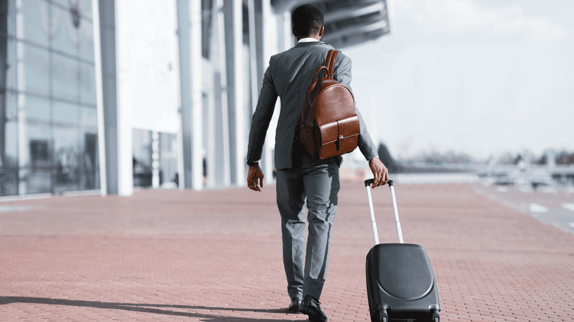 Businessman with leather backpack and suitcase walking outside an airport terminal