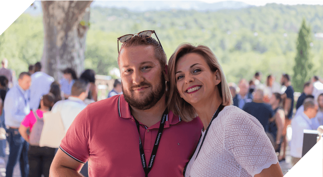 Two HOMEBOX colleagues smiling together at an outdoor company gathering with attendees behind
