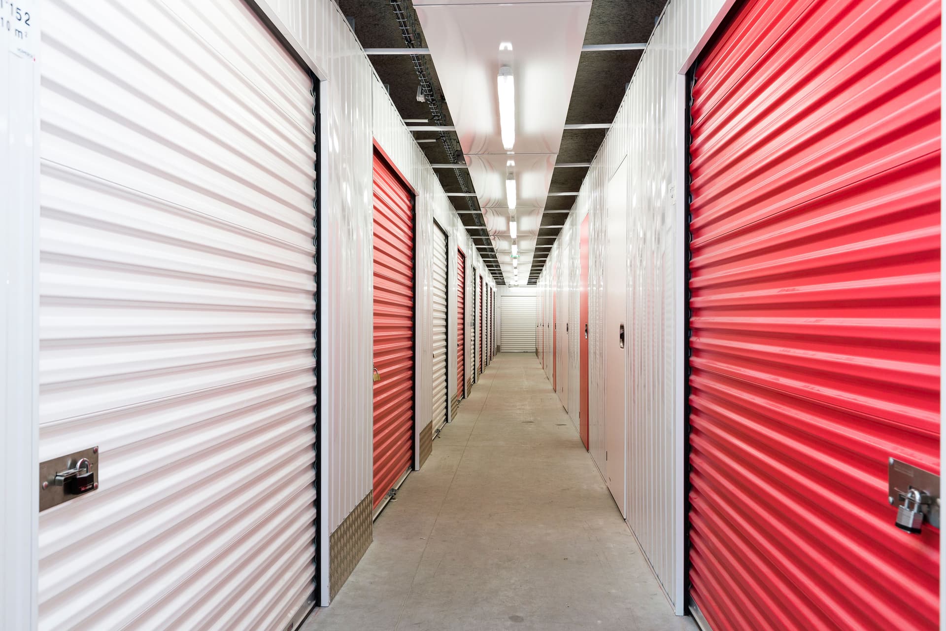 Couloir de box de stockage du centre HOMEBOX Andorra la Vella avec portes roulantes rouges et blanches."