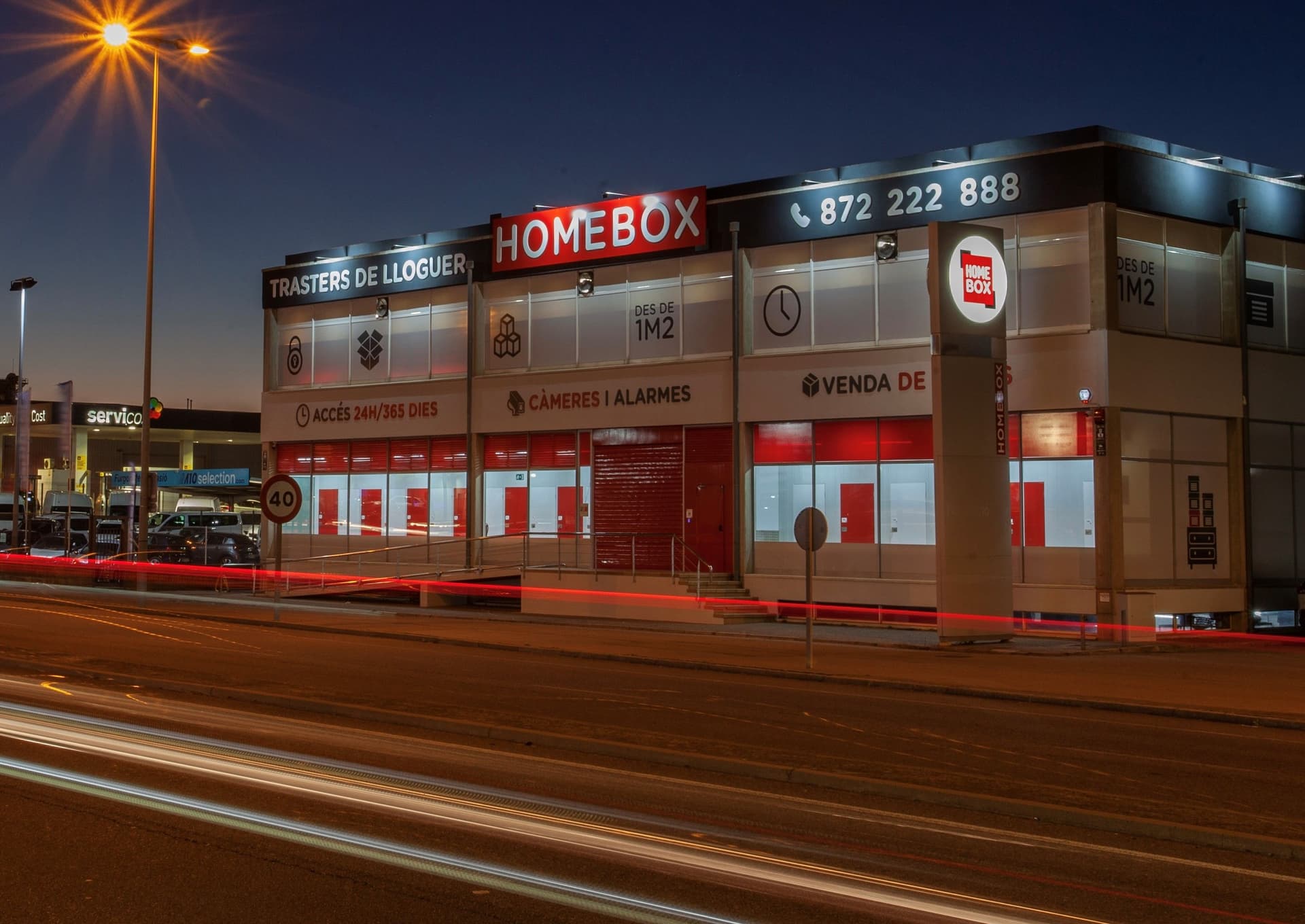 Illuminated HOMEBOX storefront at night with light trails on the road at HOMEBOX Girona, N-II a, 19, Fornells de la Selva