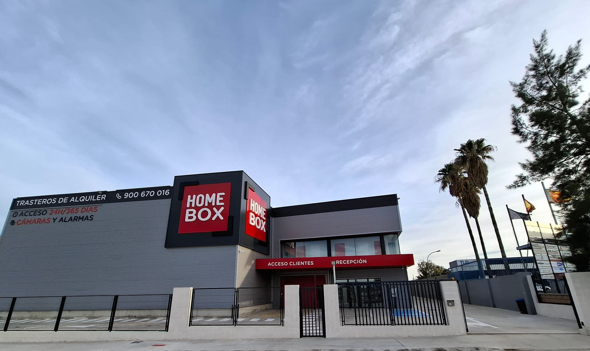 Edificio moderno con doble cartelería HOMEBOX y palmeras del centro HOMEBOX Valencia, Avng Comarques del Pais Valencía 61, Quart de Poblet